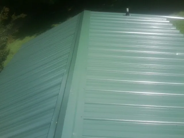 New green metal panels meeting at the ridge of a roof — Flat Roof Repair work by our crew in Glassport