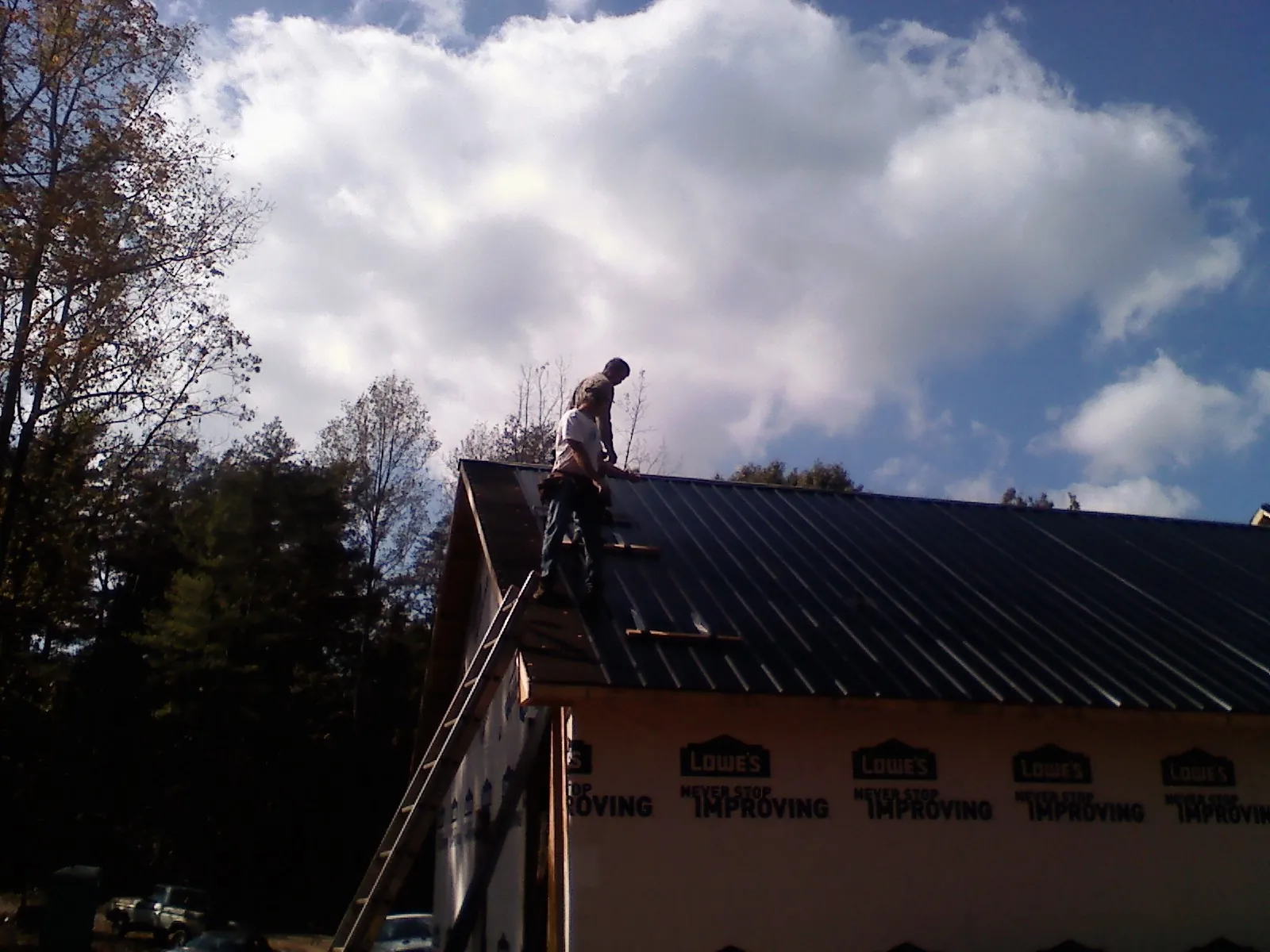 Roofer fastening dark metal panels high against a cloudy sky, from a Roof Inspection job in Glassport