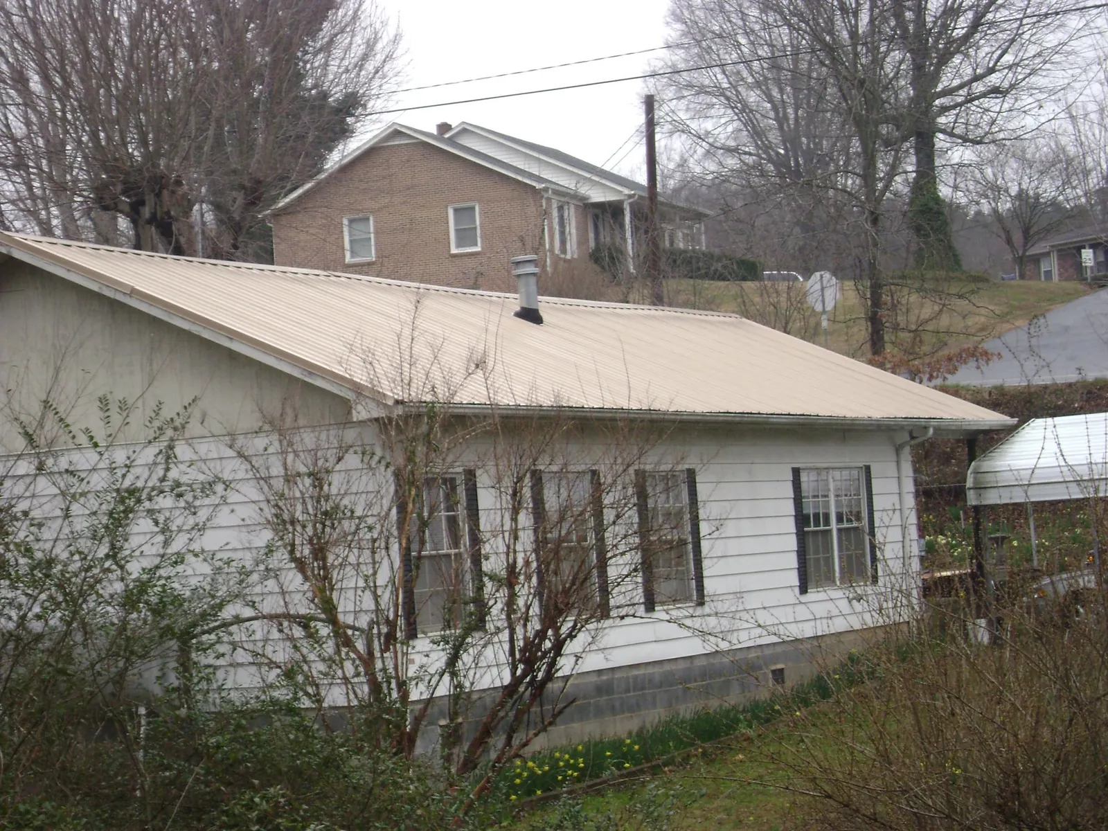 Tan metal roof on a white sided house set into a hillside — Commercial Roofing by Roofing Brothers in Glassport